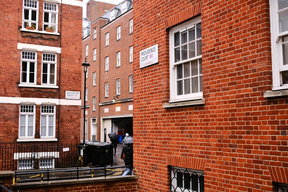 A view of a narrow urban street with red brick buildings on both sides, featuring multiple white-framed sash windows and street signs indicating Balderton Street and Providence Court in Earls Court. I
